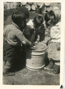 Image of Eskimo [Inuit] children tasting molasses in barrels brought by MacMillan